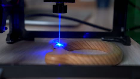 desktop laser wood burning machine uses a blue laser beam to inscribe name on surface of childrens wooden toy. home production of teethers and rattles for babies