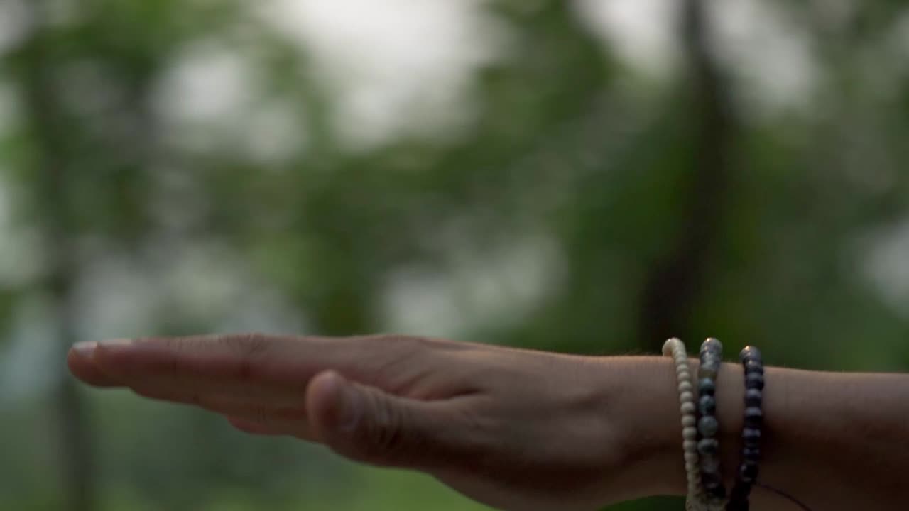 A close-up shot of a hand, adorned with multiple dark bracelets, extended slightly out of a moving vehicle's window
