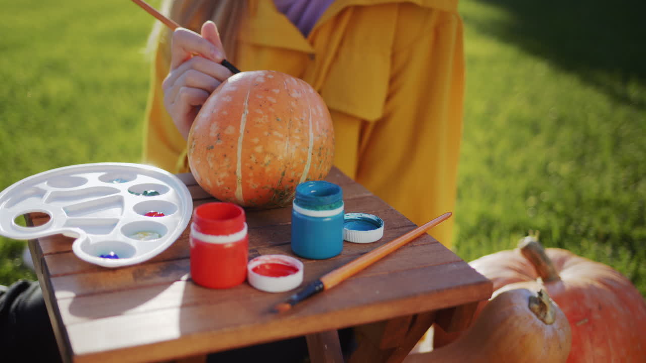 un niño pinta una calabaza, prepara decoraciones para halloween. se sienta en el césped en el patio trasero de la casa