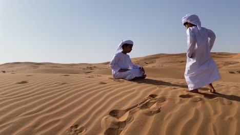 two emarati children playing with sand in the desert