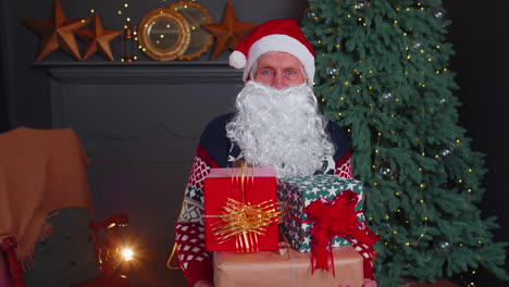 senior grandfather parodies santa claus presenting christmas gift box, holidays celebration at home