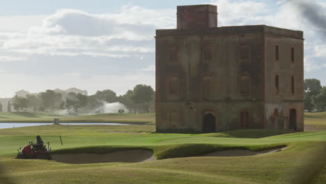 un trabajador tosco de golf saca la cortadora de césped del pozo de arena cerca de la antigua villa durante un amanecer temprano en la mañana
