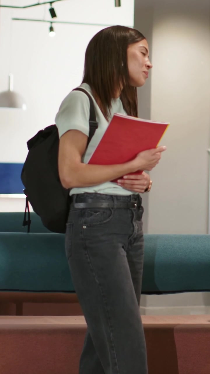 Video verticale: Sentendo qualcuno, studente con zaino che gira la testa, riponendo una cartella rossa in un salotto.