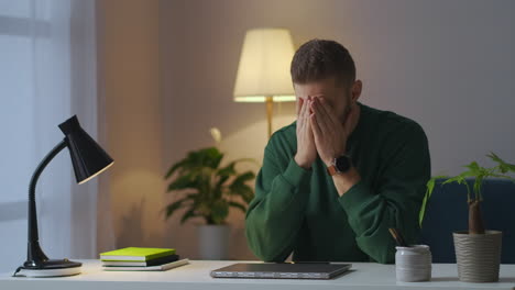 trabajo remoto en la oficina de casa por la noche cansado hombre está cerrando la computadora portátil y frotando las templas exceso de trabajo y dolor de cabeza de aparatos electrónicos