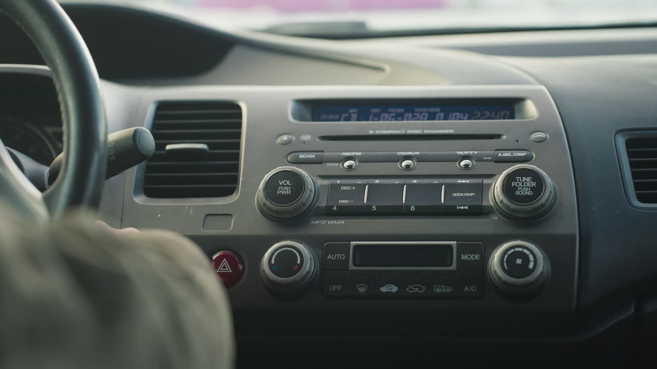 driver inside parked vehicle turns off car as dashboard radio display light fades, hand visible on ignition near hazard button, interior panel with buttons, dials, and screen in clear focus