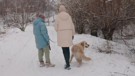 two women and a dog walking through a snow-covered path