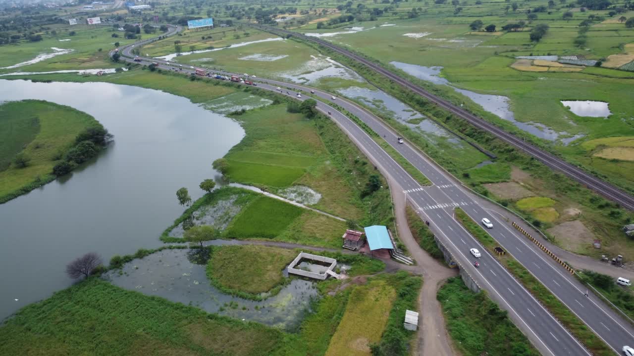 멀리 산으로 둘러싸인 고속도로 옆 철로와 4차선 고속도로에서 지나가는 자동차와 대형 차량 옆에 물에 잠긴 광활한 농지를 촬영한 영화 같은 공중 드론
