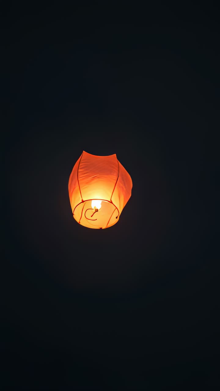 Video verticale: lancio di una lanterna arancione, che si alza di notte, anello di metallo, fiamma, luna, nuvole