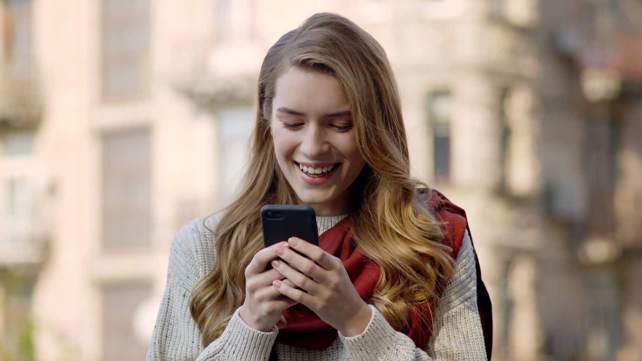 mujer feliz enviando mensajes de texto por teléfono al aire libre. niña sonriente recibiendo un mensaje en la calle