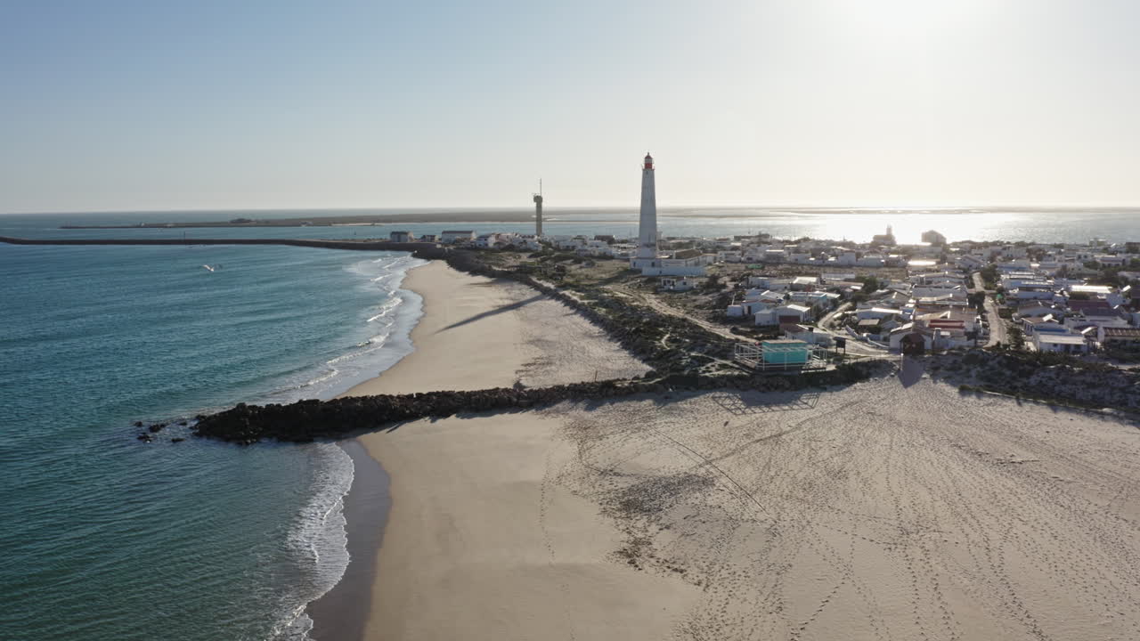 Aerial rotation shot of Ilha de Farol island town with lighthouse, small colorful houses and ocean front