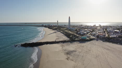 aerial rotation shot of ilha de farol island town with lighthouse, small colorful houses and ocean front