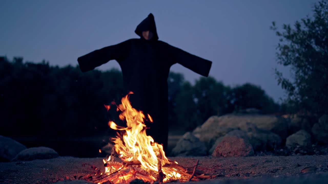 Witch in black near bonfire. Mystical witch walking around bonfire