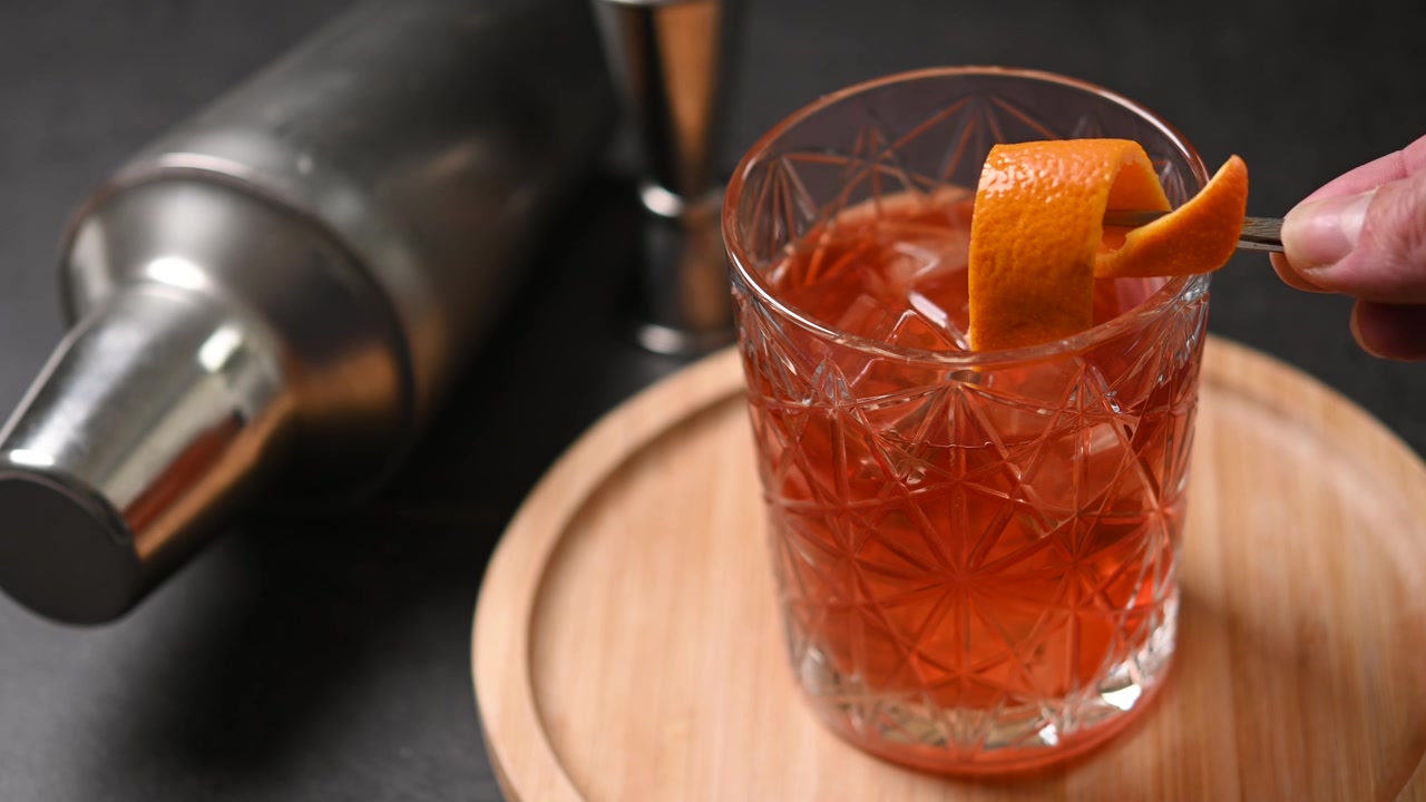 Barman che guarnisce un cocktail Old Fashioned con scorza d'arancia
