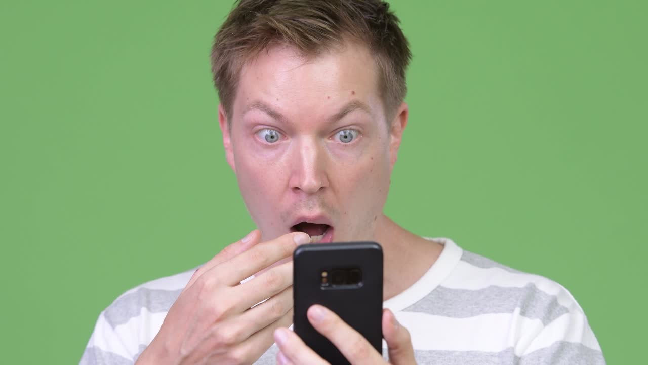 Young handsome man using phone and looking shocked