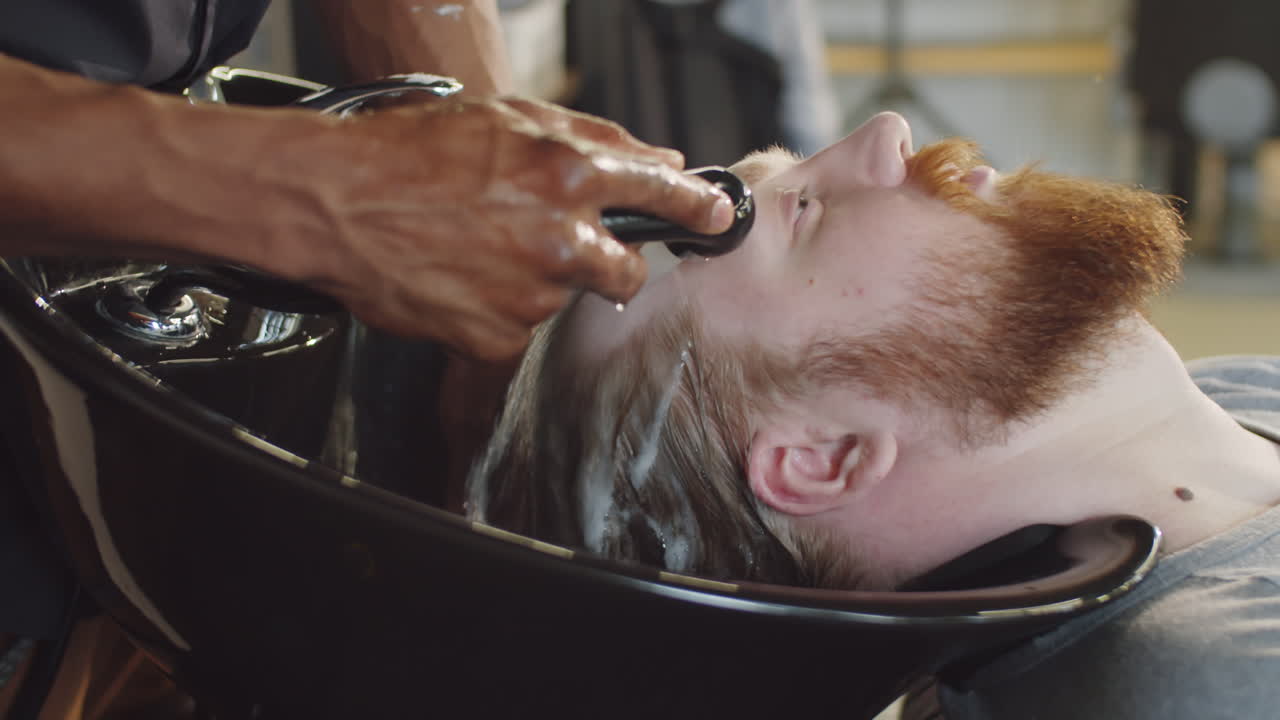 Barbiere che risciacqua lo shampoo dai capelli di un uomo