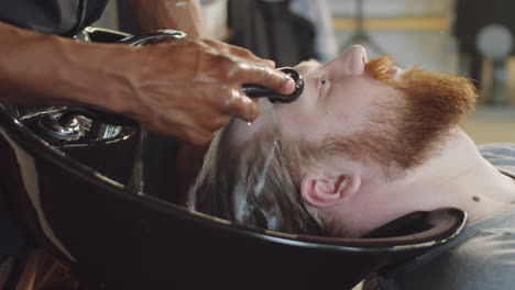 barber rinsing out shampoo from hair of man