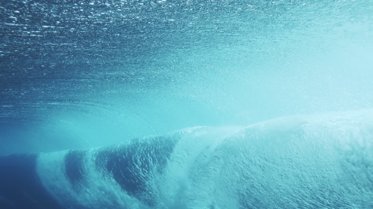 Rearview underwater slow motion of barreling wave foaming into tube rolling with whitewash