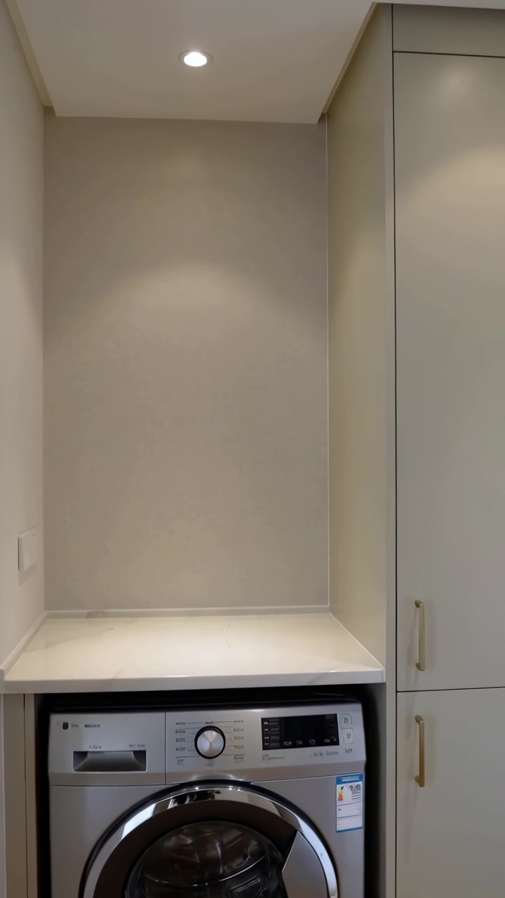 Video verticale: Telecamera che si inclina mostrando una lavatrice a carica frontale in un angolo di casa, rivelando una nicchia e un armadietto