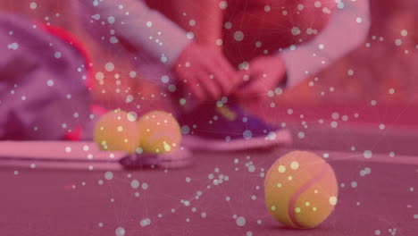 woman kneeling on red tennis court gathering yellow balls, showing sports technology data overlay
