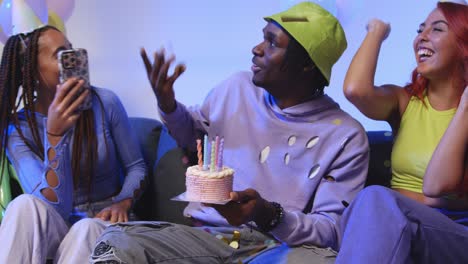 studio shot of gen z friends celebrating man's birthday with party cake and candles sitting on sofa 1