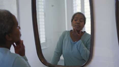 African-american-senior-woman-looking-at-mirror-in-bathroom