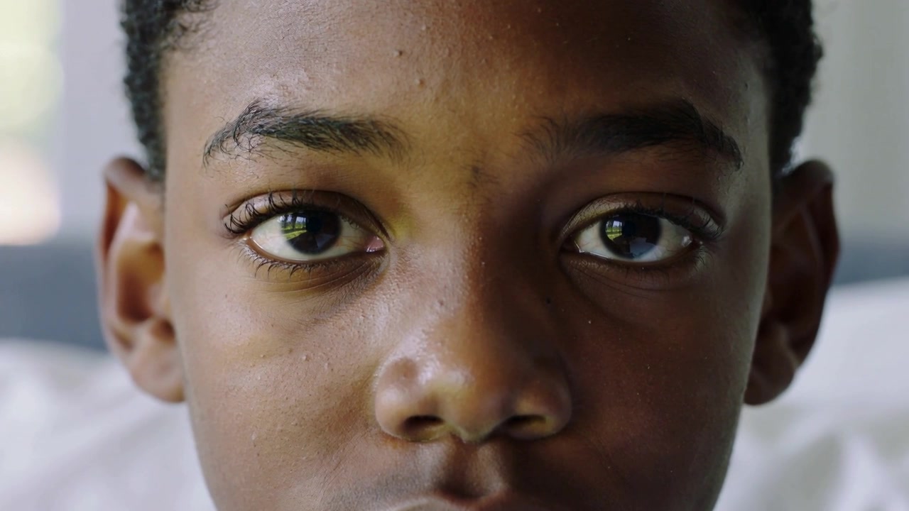 Piscando com a luz suave do dia, adolescente masculino fazendo movimentos com os olhos e fechando-os na cama, com travesseiro.