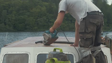 los jóvenes configuran seres lijadoras de banda lijando el techo de la timonera de un barco de madera.