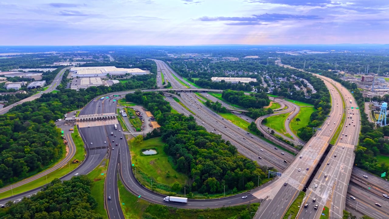 Evening light highway interchange and distant horizon, New York. Wide aerial drone shot of expansive road network under cloudy sky and golden sunlight rays. Garden State Parkway