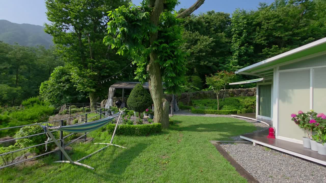 A beautiful view of the luxury Glam Tree glamping resort in South Korea, featuring modern cabins, a relaxing hammock, and a landscaped garden nestled in a peaceful green mountain valley