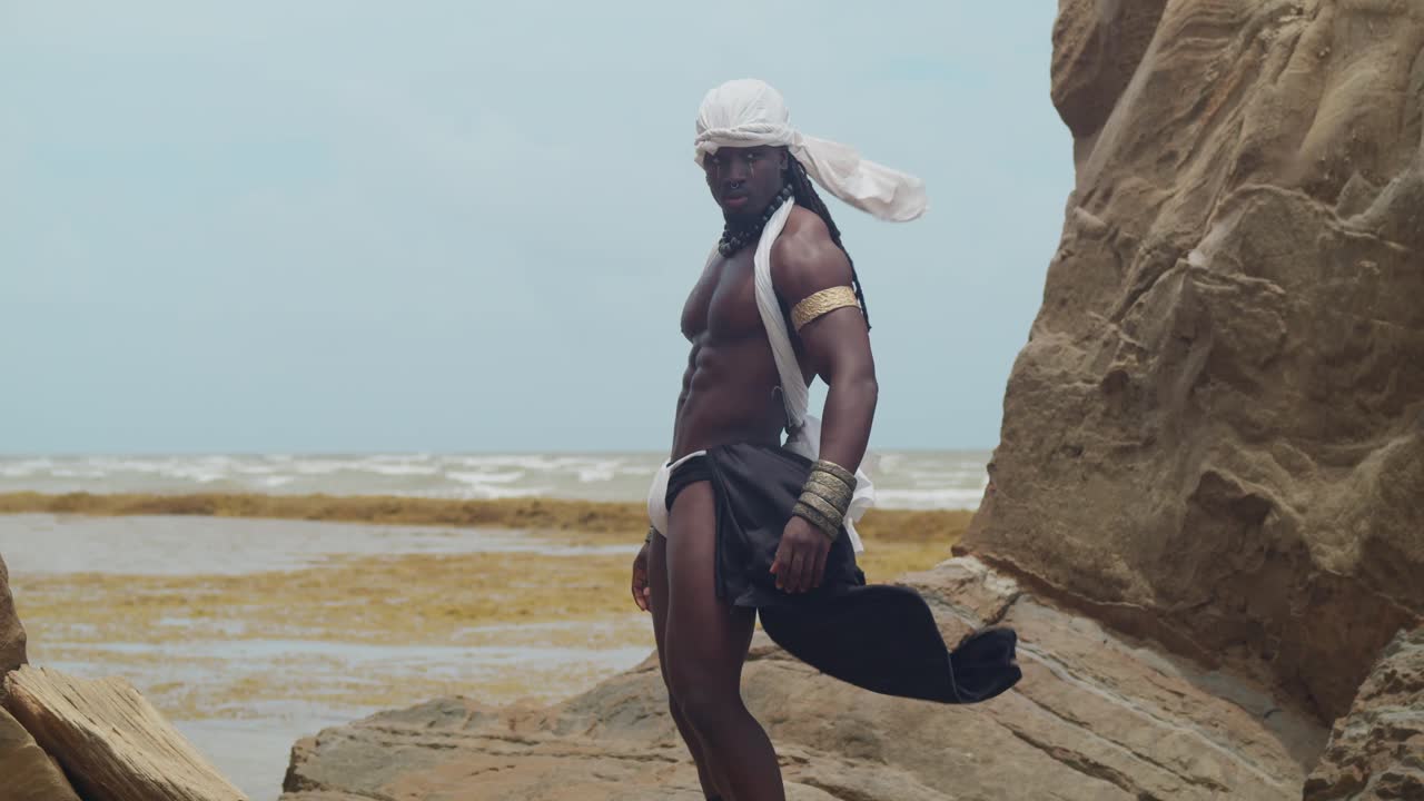 A male cosplayer, his dark skin and muscles prominent on the beach.