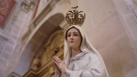 close up of crowned virgin mary statue with rosary in quiet sacred church setting