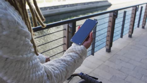 Mixed-race-man-with-dreadlocks-riding-a-bicycle-in-the-street-using-smartphone