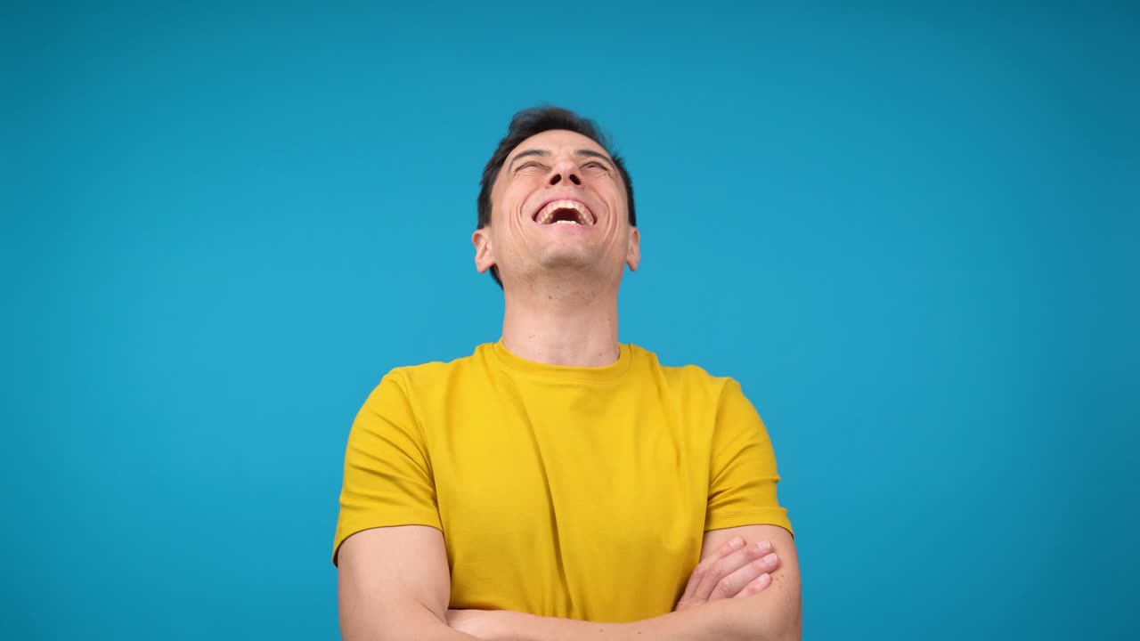Man laughing heartily with eyes closed in a yellow shirt against a blue background