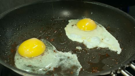 two raw eggs with bright yellow yolks fry in hot oiled pan in kitchen