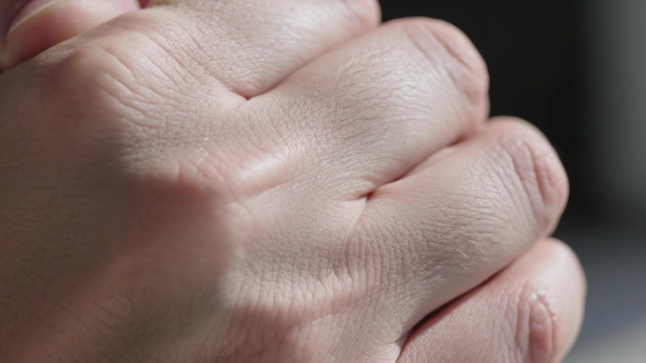 Kamera fanger en voksen hånd som knytter fingrene i et roms interiør, med detaljer av knokene.