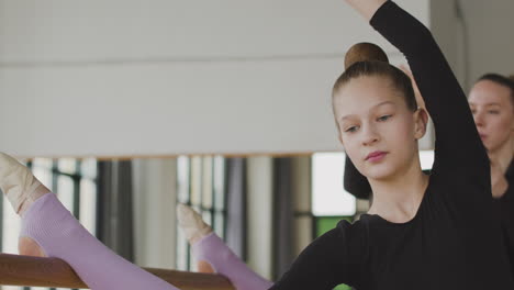 close up view of gymnastic blonde girl rehearsing a ballet move in front of ballet barre