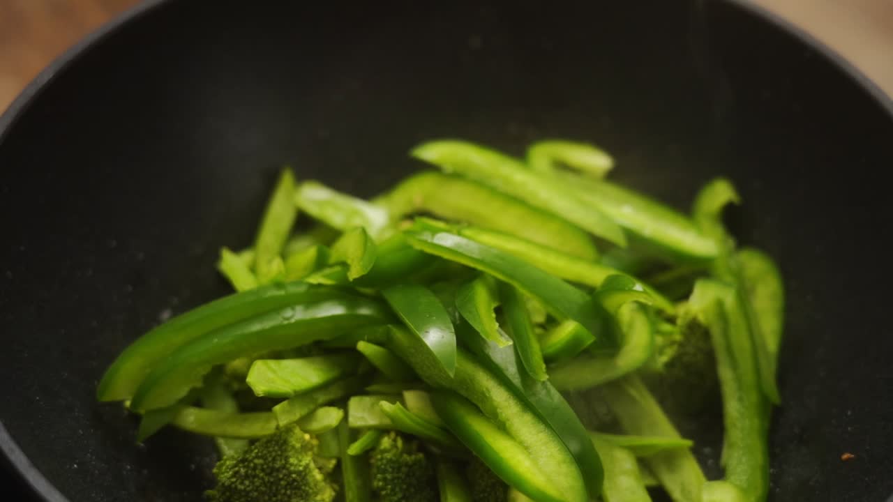 cocinero anónimo agregando pimientos cortados a brócoli y frijoles en sartén