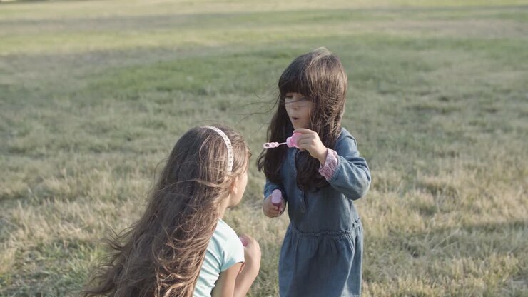 Niñas latinas lindas soplando burbujas entre ellas en el parque.