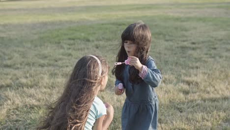 cute latin little girls blowing bubbles on each other in the park