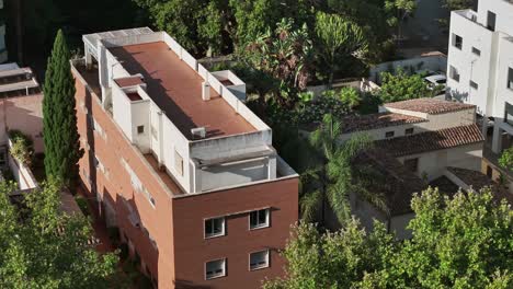 aerial fly near a red brick apartment block among trees and surrounding suburban houses, spain