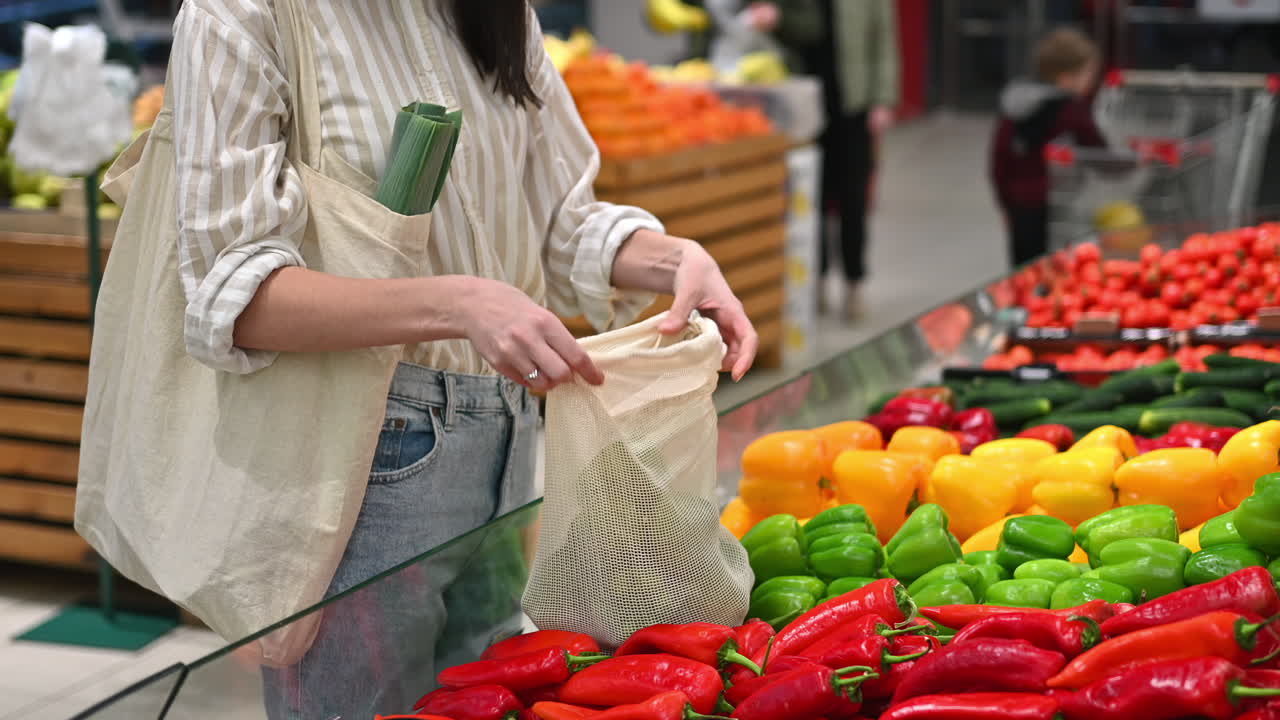 Mujer recogiendo pimientos en una bolsa reutilizable en una tienda. Temática de ecología y Día de la Tierra. Cámara lenta