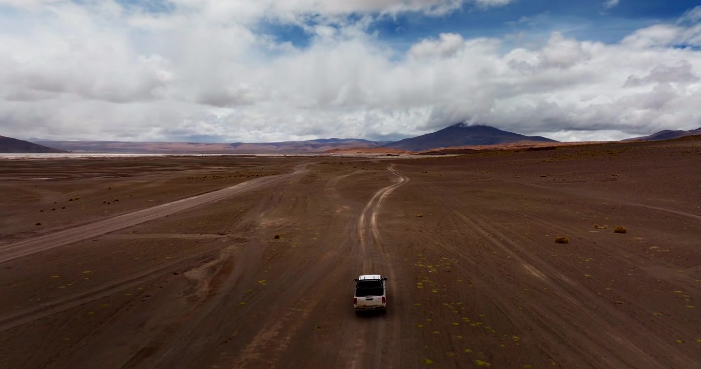 Drone che segue un SUV in spedizione fuoristrada attraverso il terreno arido e vasto del deserto di Siloli in Sud America, Bolivia