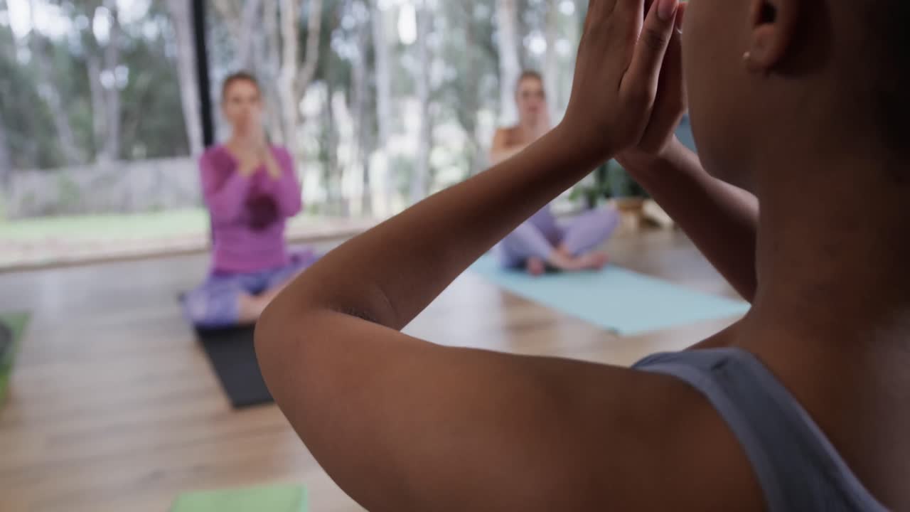 Donne di diverse etnie concentrate che meditano insieme sui tappetini in una lezione di yoga con istruttrice, al rallentatore