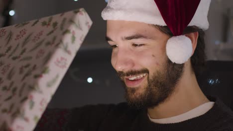 hombre conmocionado y sorprendido abriendo el regalo de navidad que ilumina la cara