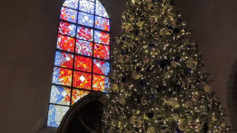 tall christmas tree inside a church standing next to a colorful stained glass well illuminated