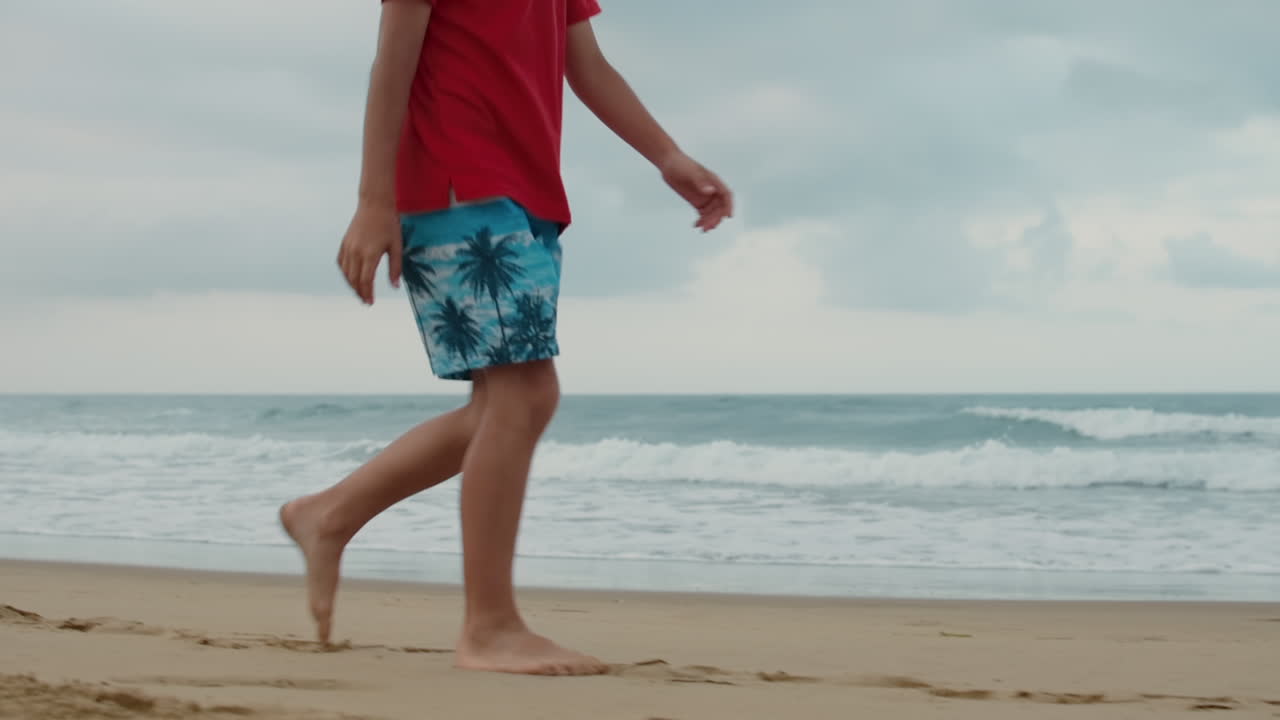 Unknown boy enjoying summer at beach. Unrecognizable guy walking along seaside.