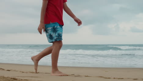 Unknown-boy-enjoying-summer-at-beach.-Unrecognizable-guy-walking-along-seaside.