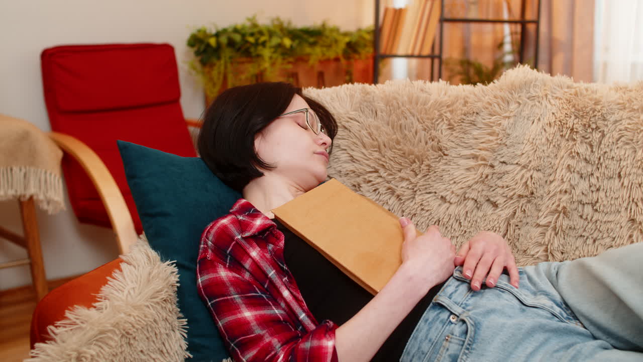 Young woman falling asleep with book in hand at home peaceful expression and tired body language