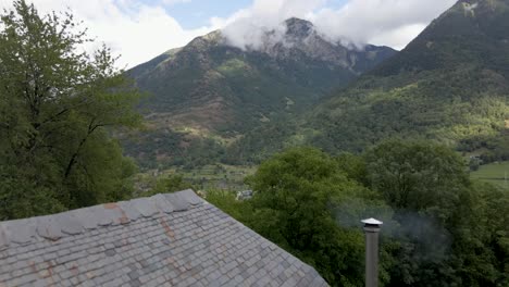 The-drone-begins-with-a-view-of-a-secluded-cabin-nestled-in-the-serene-woods,-and-then-gracefully-ascends-to-reveal-the-charming-Spanish-town-in-the-background,-set-amidst-the-Pyrenees-mountains