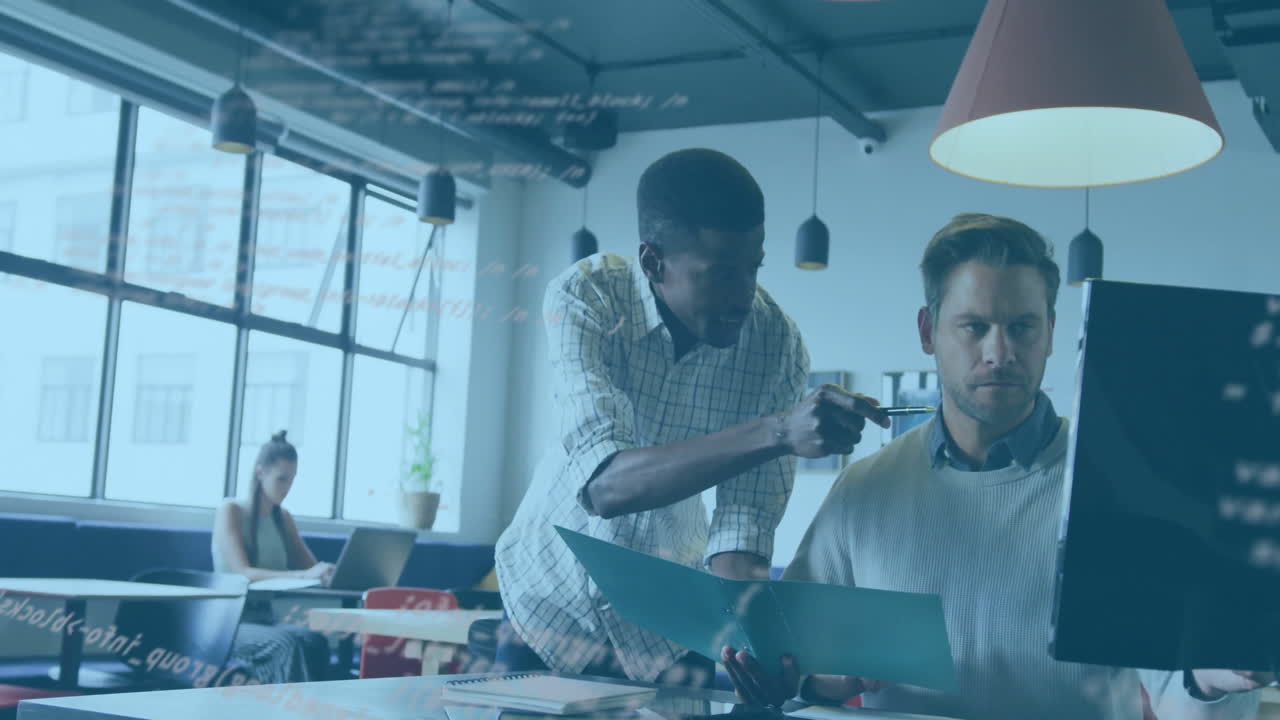 Two colleagues leaning over desk in business office, displaying animated graph overlay above laptop